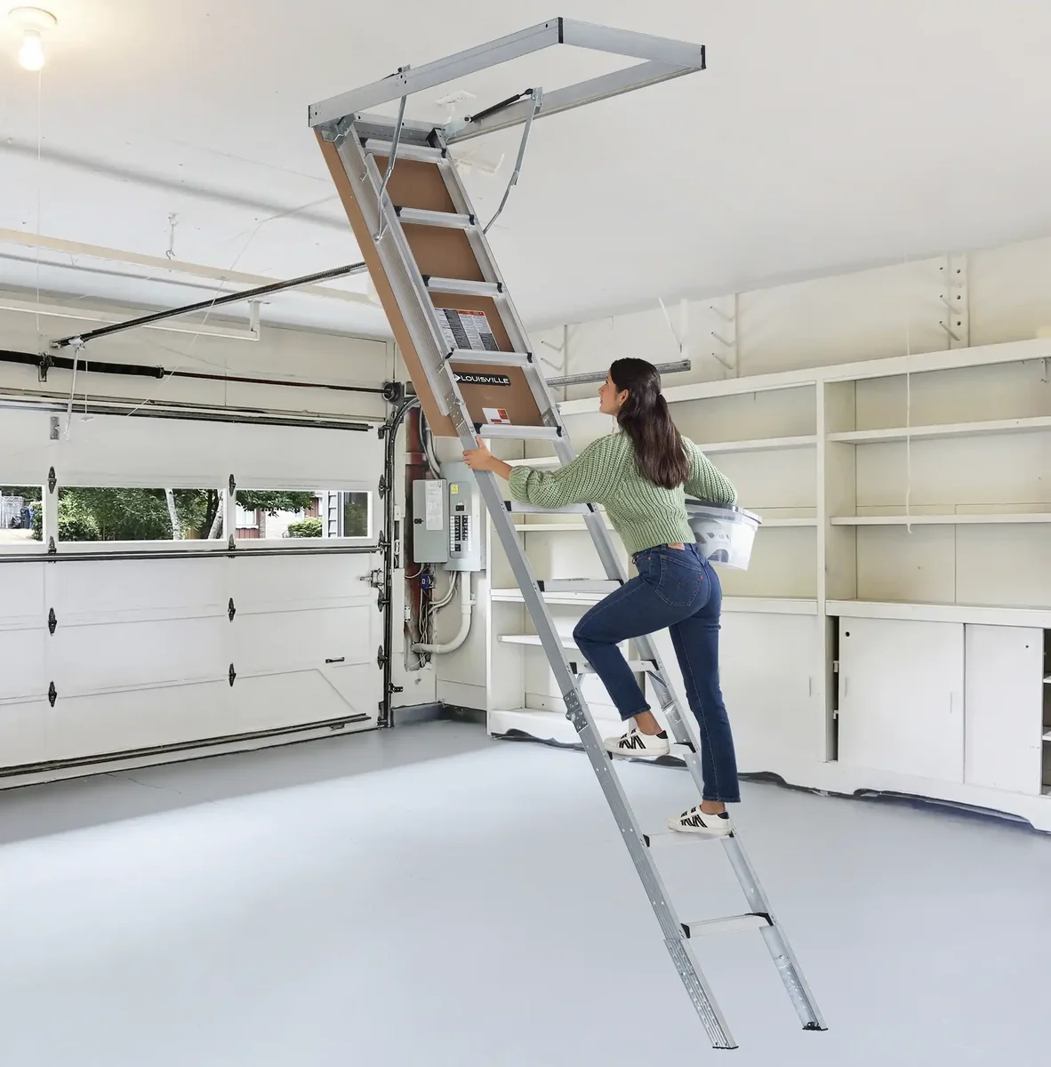 Homeowner climbing a Louisville Ladder aluminum attic ladder to reach garage storage